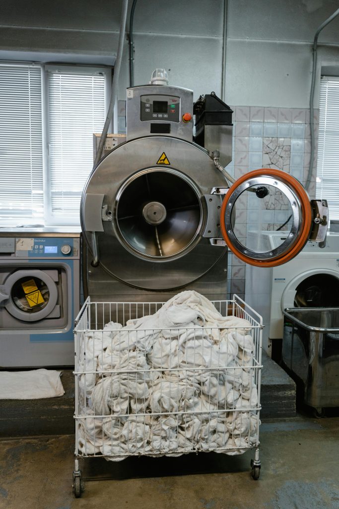Large industrial washing machine with a cart full of linens in a laundry facility.